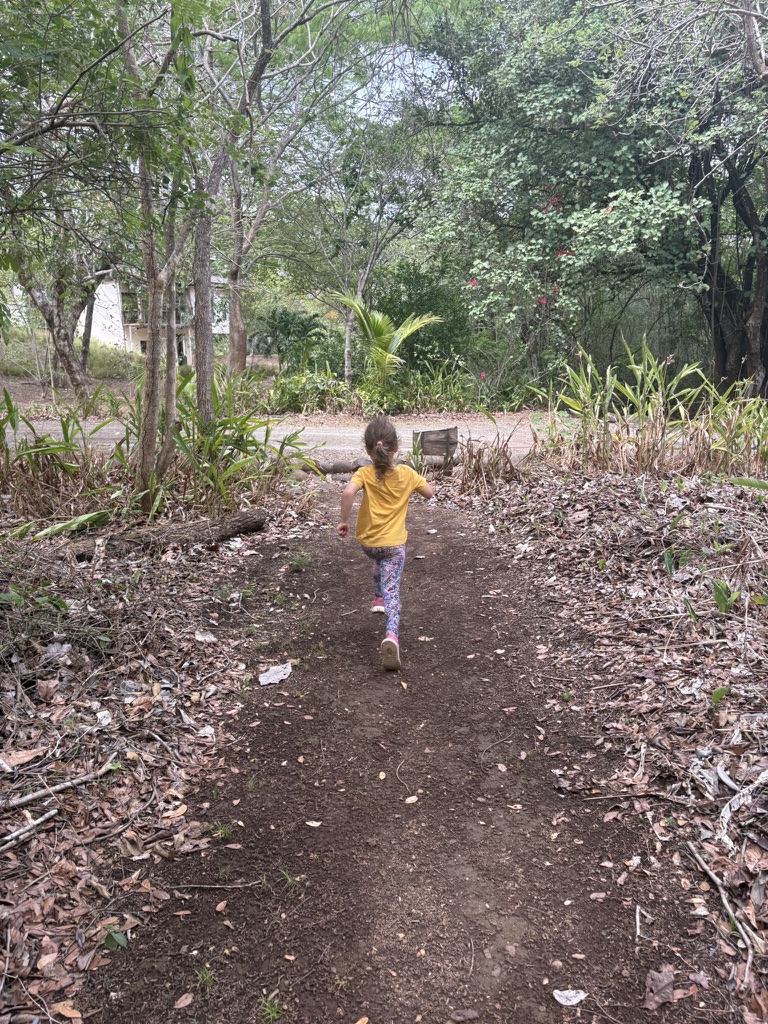 A girl in a yellow t-shirt running off down a leafy forest trail