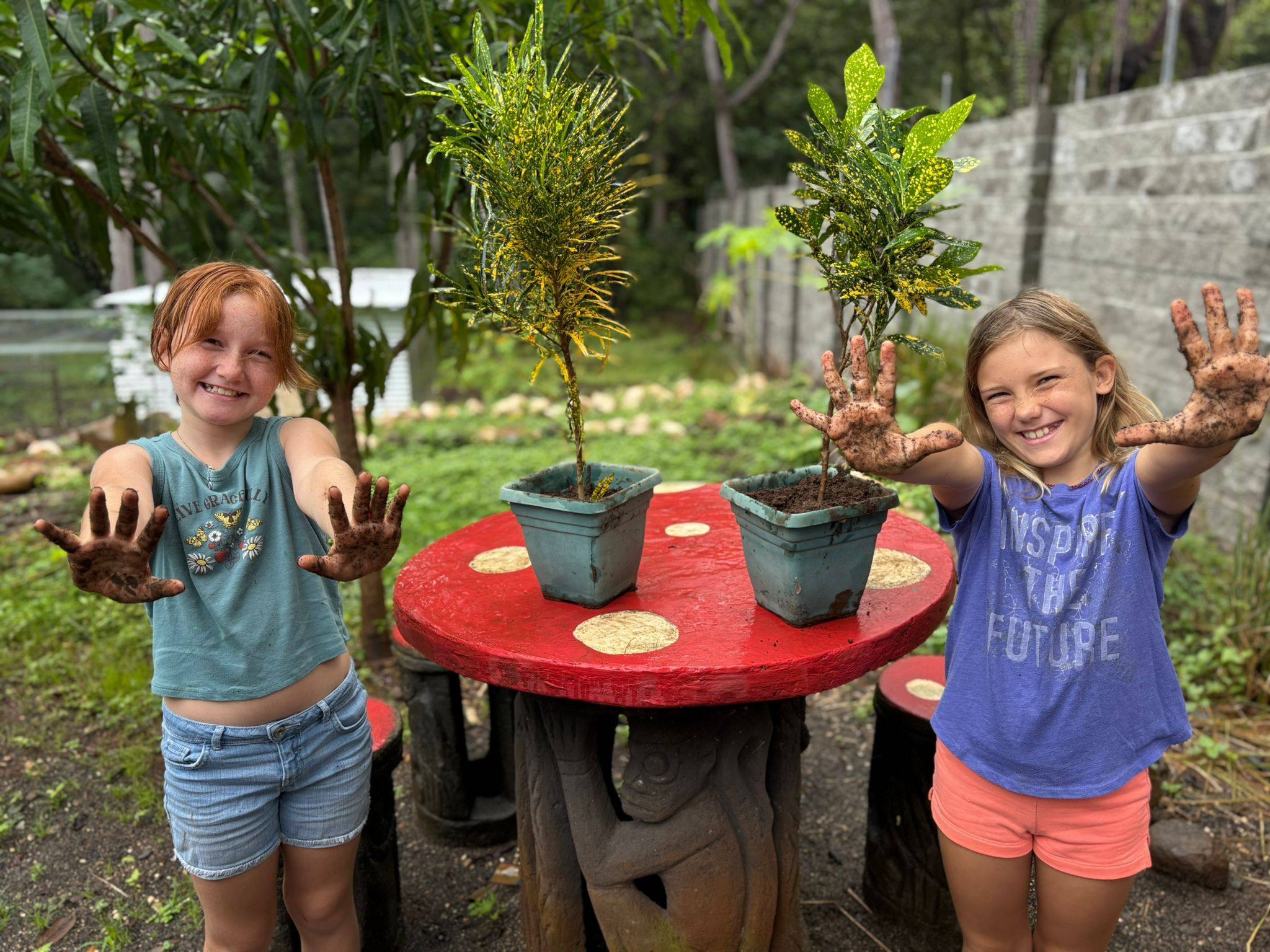 Two children grinning and holding up their mud-covered hands after planting saplings in the garden