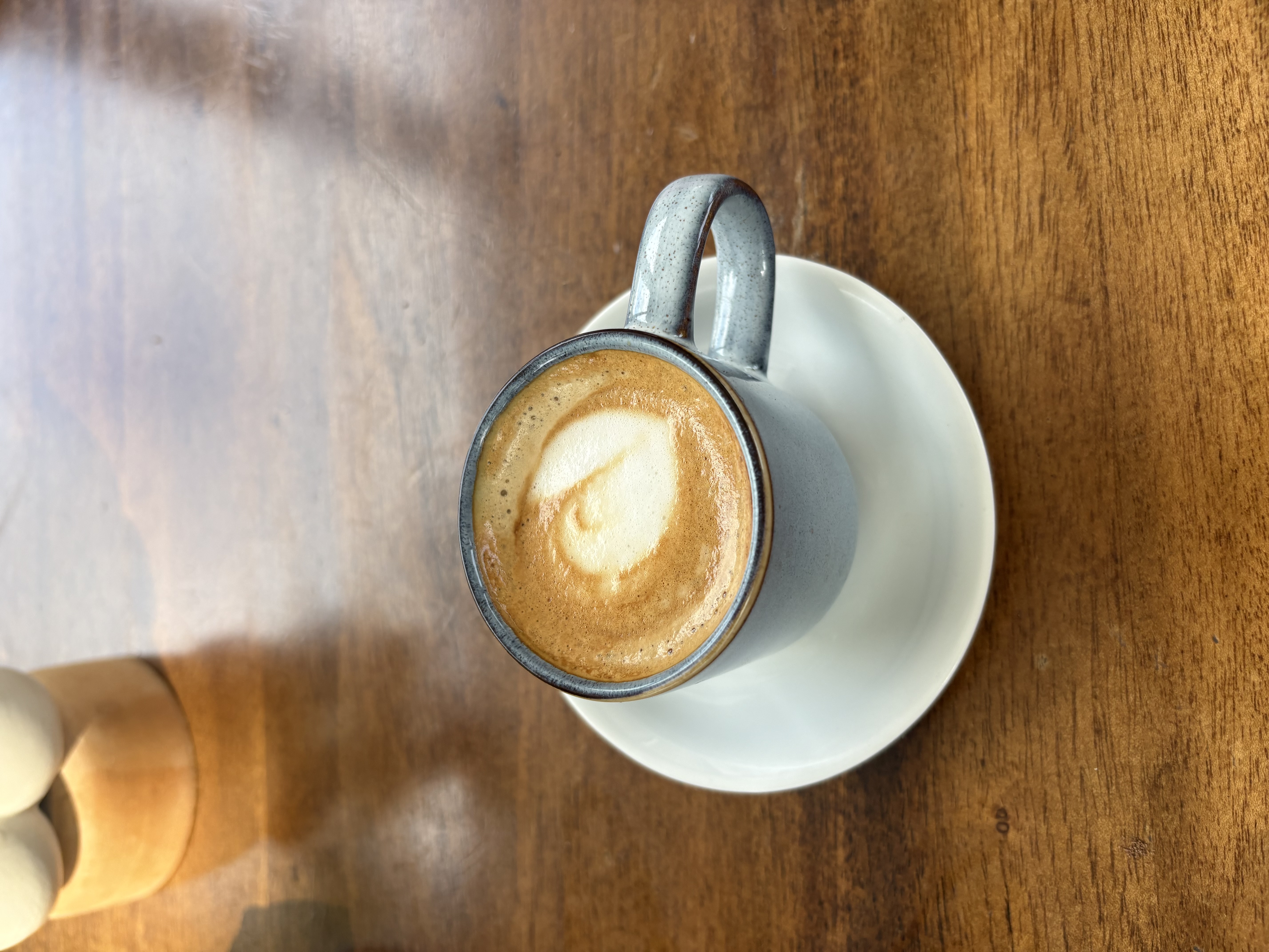 A freshly made flat white with latte art resting on a sunlit wooden table